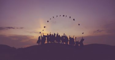Silhouettes of college graduates on a hill horizon throwing their caps in the air