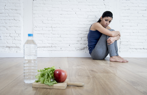young woman sitting on ground alone and worried at home suffering from eating disorder