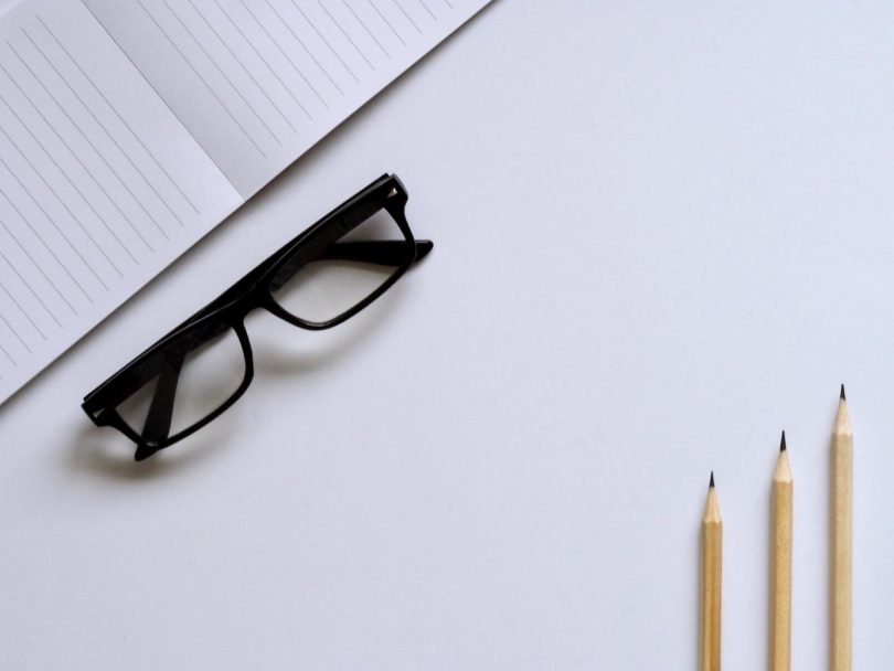 black glasses, notebook and pencils on a white desk