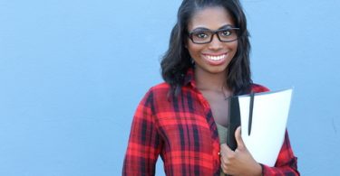 African american female college freshman holding books with a blue background