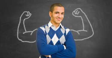 college student in blue sweater standning in front of chalk board with flexing muscles drawn on it