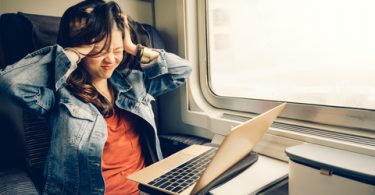 upset Asian college student sitting with her laptop on a bus