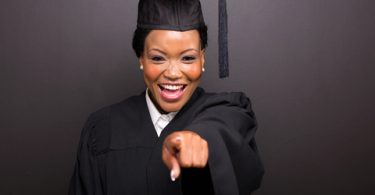 smiling female college graduate pointing isolated on black background