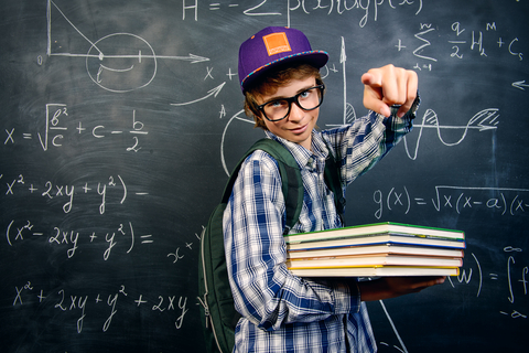 male high school student standing by a school blackboard.