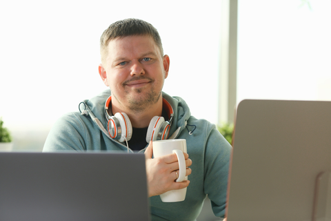 smiling male student using online education service and drink tea or coffee.