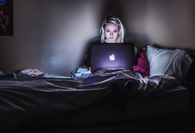 blonde college student on her laptop in the dark in her bed