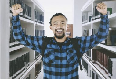 Picture of African male college student celebrating his success by lifting hands in the library