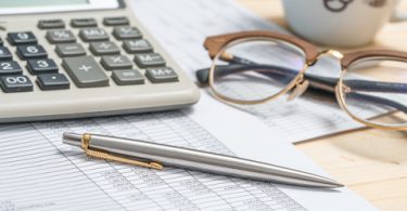 Accounting tools on a desk with calculator, pen glasses and coffee mug