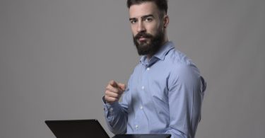 young entrepreneur student in blue shirt holding laptop and pointing