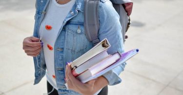 female college student standing outside wearing backpack and holding textbooks