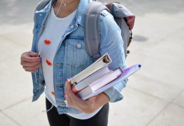 female college student standing outside wearing backpack and holding textbooks