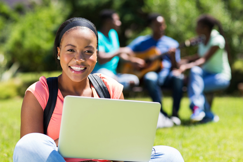 cheerful african college student using laptop outdoors