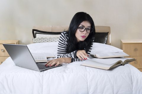 Portrait of beautiful female college student writing an essay using a laptop computer on the bed