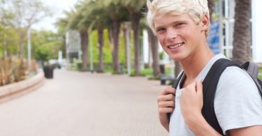 young male freshman college student on campus with backpack standing outside