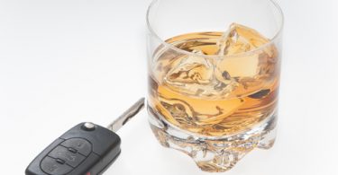 car key and alcoholic beverage with ice in a glass sitting on white background