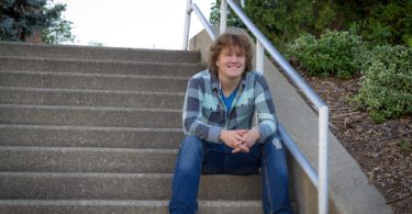 curly haired male college student smiling and sitting on steps outside