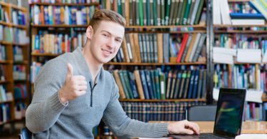 Student with laptop showing thumbs up in the university library