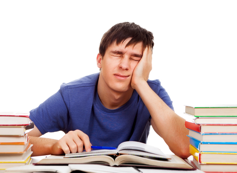 frustrated male college student sitting at desk with lots of books