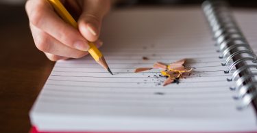 college students hand writing with a pencil on notebook with pencil shavings laying on the paper