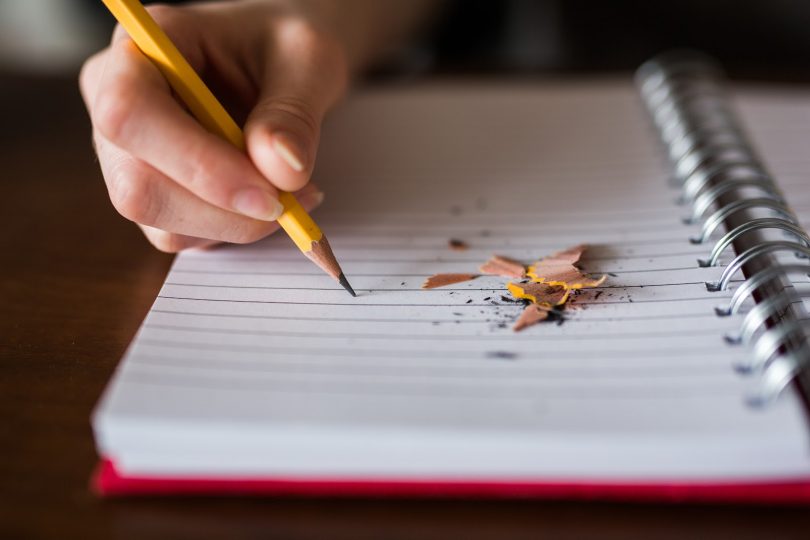 college students hand writing with a pencil on notebook with pencil shavings laying on the paper