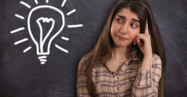 college student looking confused with light bulb next to her