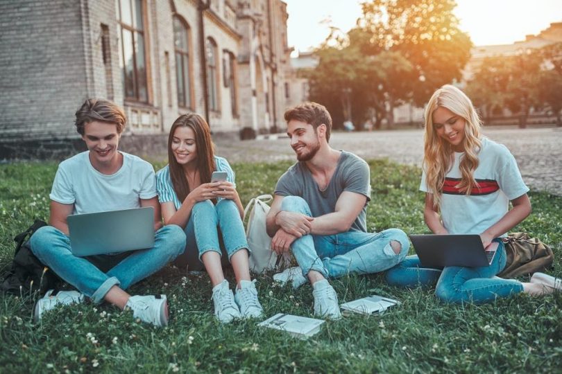 male and female college students sitting on the grass together with laptops