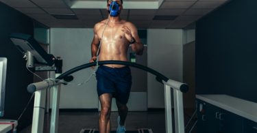 Athelte running on treadmill in shorts with face mask on
