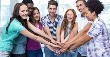 group of smiling college students all putting their hands in the middle of a circle