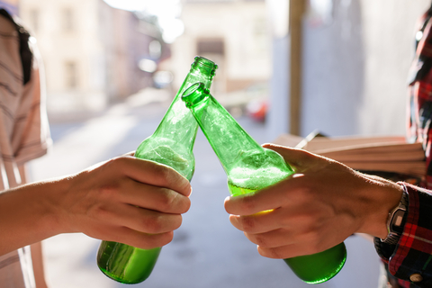 college students holding beer bottles while tapping them together