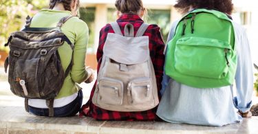 three female college students wearing backpacks while sitting on steps